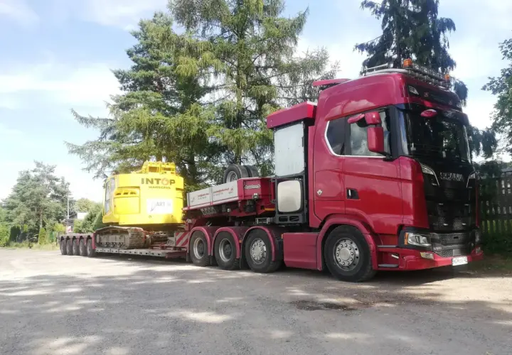 Czerwony Scania z naczepą transportuje żółtą koparkę. To typowa przesyłka dużych gabarytów, gotowa do drogi.