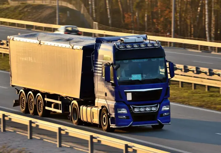Niebieska ciężarówka z naczepą jedzie autostradą. Kierowca z kodem 95 prawo jazdy wiezie towar.