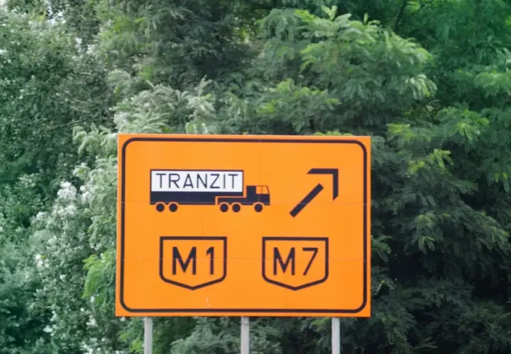 Pomarańczowy znak drogowy na Węgrzech informuje o tranzycie ciężarówek na M1 i M7. Upewnij się, że masz winietę, by uniknąć mandatu.