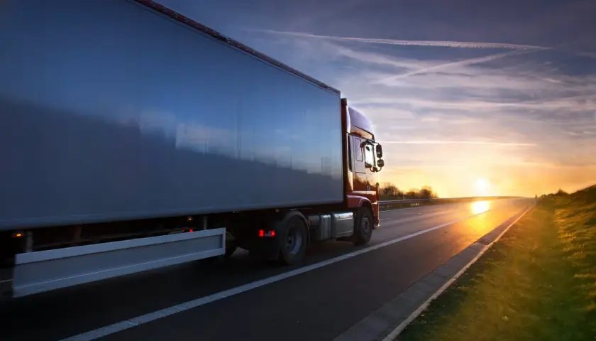 Kierowca zawodowy wyrusza w trasę o zachodzie słońca. Ciężarówka jedzie autostradą, a niebo jest pełne smug po samolotach.