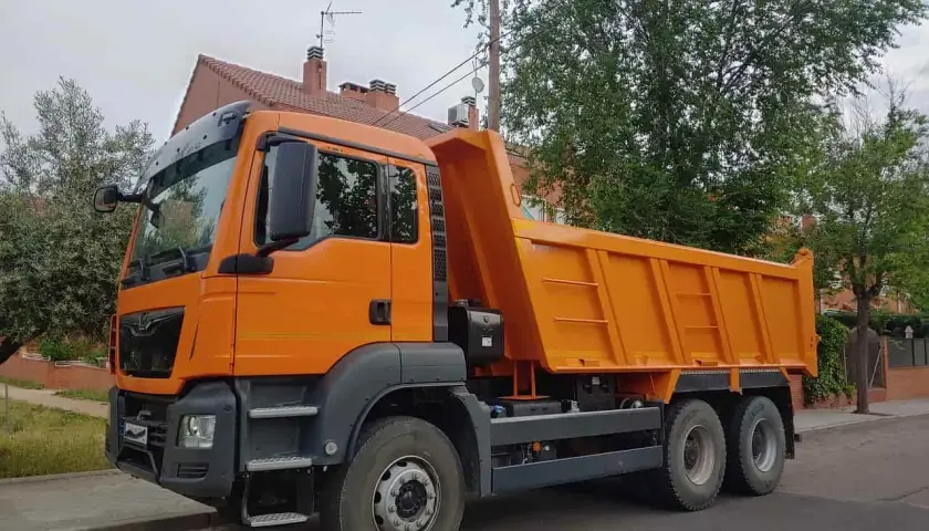 Pomarańczowa wywrotka na tle drzew i domu. Czy można mieć kat C bez B? Tak, to możliwe, jeśli masz odpowiednie szkolenie.