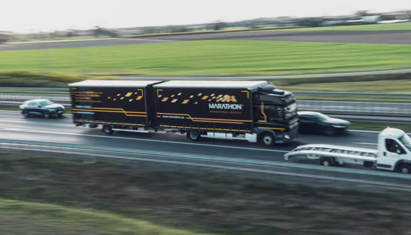 Ciężarówka Marathon International Logistics na autostradzie, obok samochód osobowy i laweta. To transport bilateralny przykład.