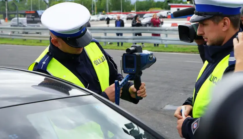 Policjant mierzy prędkość, grozi zabrane prawo jazdy za prędkość. Inny funkcjonariusz filmuje akcję.