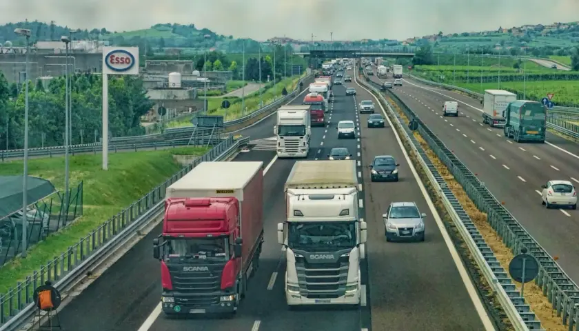 Kierowca zawodowy w trasie, ciężarówki na autostradzie. W tle znak Esso i zielone wzgórza.