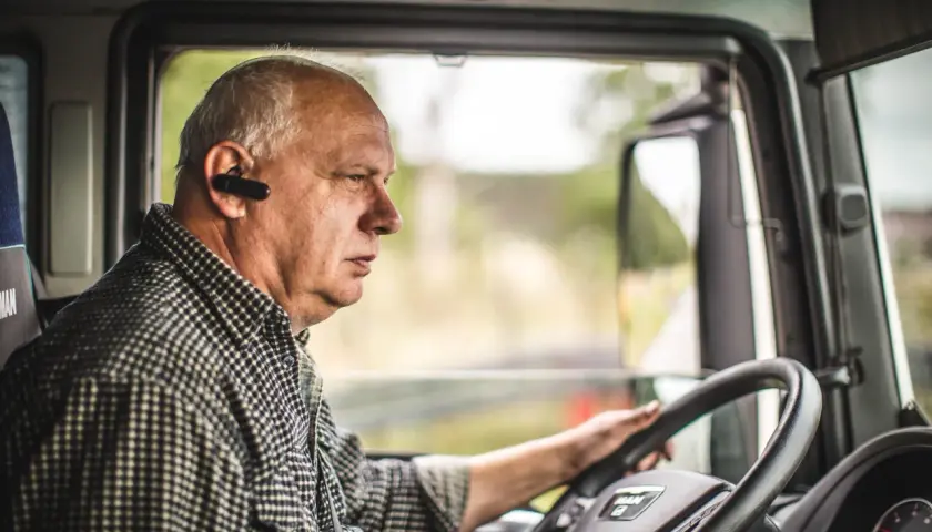 Kierowca ciężarówki w słuchawce Bluetooth, skupiony na drodze. Przestrzega rozporządzenie 561 czas pracy kierowców, dbając o bezpieczeństwo.