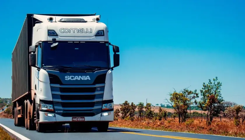 Biała ciężarówka Scania z naczepą jedzie po pustej drodze, zapowiadając zasłużoną pauzę weekendową.