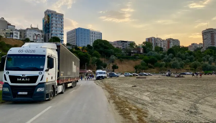 Ciężarówka MAN z naczepą na drodze, w tle budynki i plaża. Idealne miejsce na przerwę i zaplanowanie jadłospisu dla kierowcy tira.