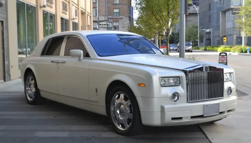 Biały Rolls-Royce, idealny na umowę transportu okazjonalnego, lśni na tle miejskiej architektury.