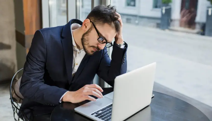 Zestresowany mężczyzna w garniturze pracuje przy laptopie, próbując skrócenie pauzy do 7 godzin.