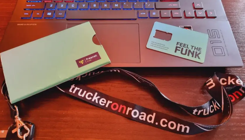 Karta SIM "Feel the Funk" i klucze na smyczy "truckeronroad.com" leżą obok laptopa. Czas na pauzę 45h bez karty w tachografie.