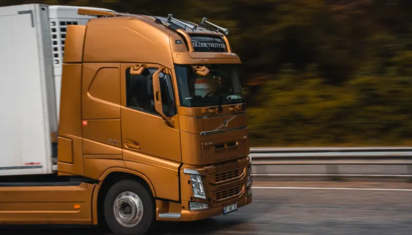 Złoty ciągnik siodłowy z naczepą jedzie drogą. Prawo przewozowe reguluje takie transporty, zapewniając bezpieczeństwo i płynność ruchu.