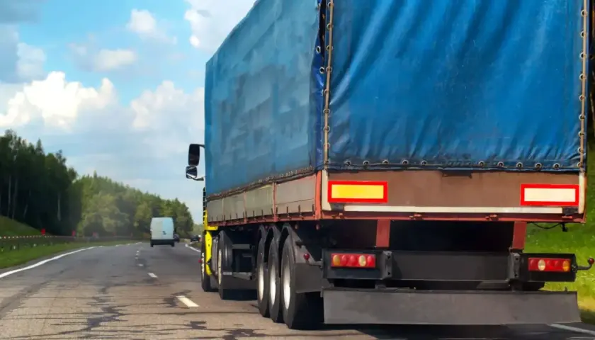 Ciężarówka z niebieską plandeką jedzie drogą. Kierowca uważa na zakaz jazdy na Węgrzech, by uniknąć kary.
