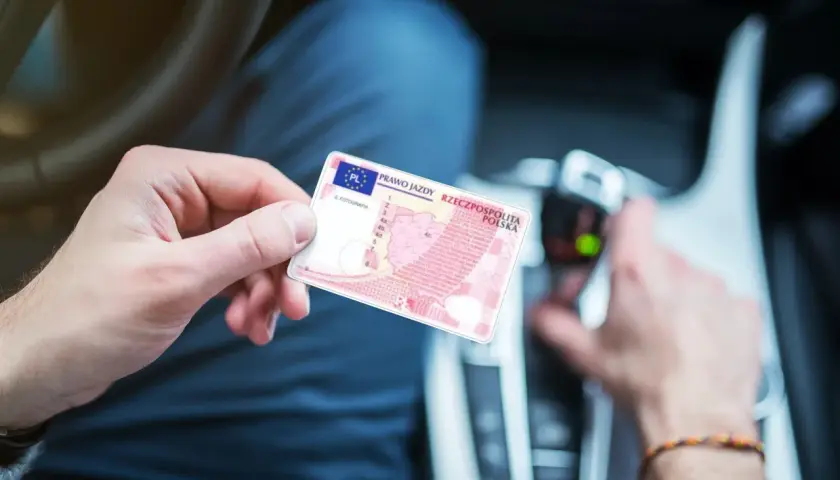 Osoba trzyma polskie prawo jazdy. W tle widać wnętrze samochodu, co sugeruje, że może to być dokument potrzebny do prowadzenia pojazdu, gdy posiada się prawo jazdy spoza Unii Europejskiej.