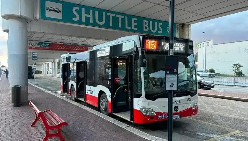 Autobus wahadłowy czeka na pasażerów pod znakiem "SHUTTLE BUS". Drzwi otwarte, gotowy do przewozu.