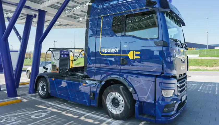 Niebieska ciężarówka elektryczna MAN eTGX z logo "epower" ładuje się pod panelem słonecznym. To przyszłość transportu, zgodna z normą euro 7.