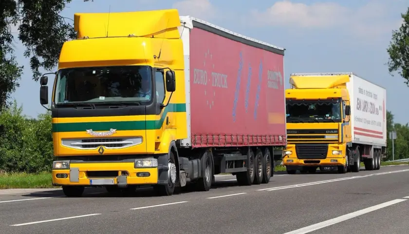 Dwa żółte ciężarówki jadące drogą. Kierowcy wykonujący przewozy drogowe powinni wiedzieć, ile godzin trwa szkolenie okresowe.