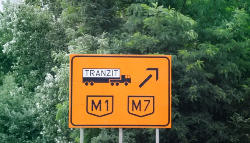 Pomarańczowy znak drogowy na Węgrzech informuje o tranzycie ciężarówek na M1 i M7. Upewnij się, że masz winietę, by uniknąć mandatu.