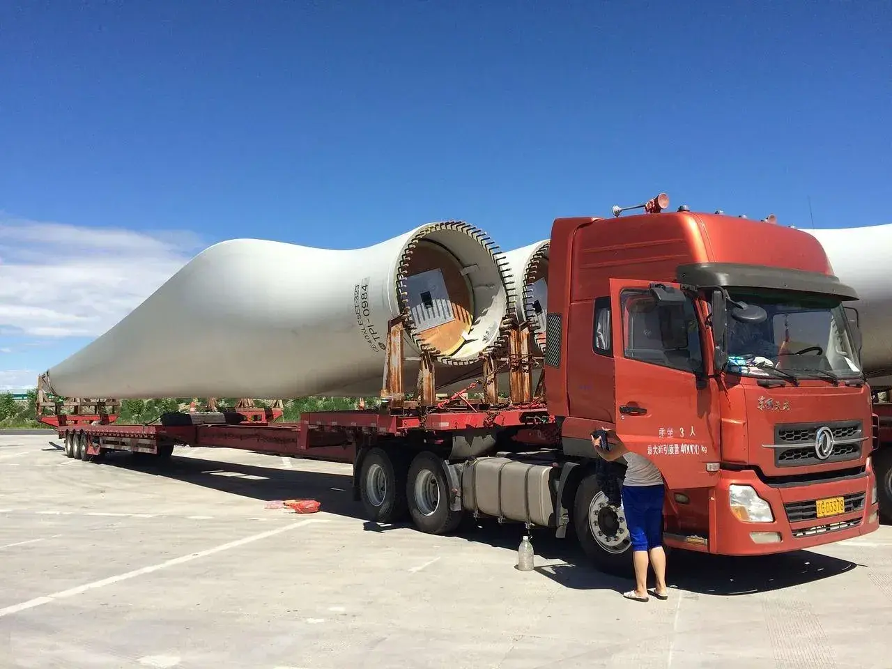 Ciężarówka transportuje łopatę turbiny wiatrowej. To ważny element w kraju tranzytowym, czekający na dalszą podróż.