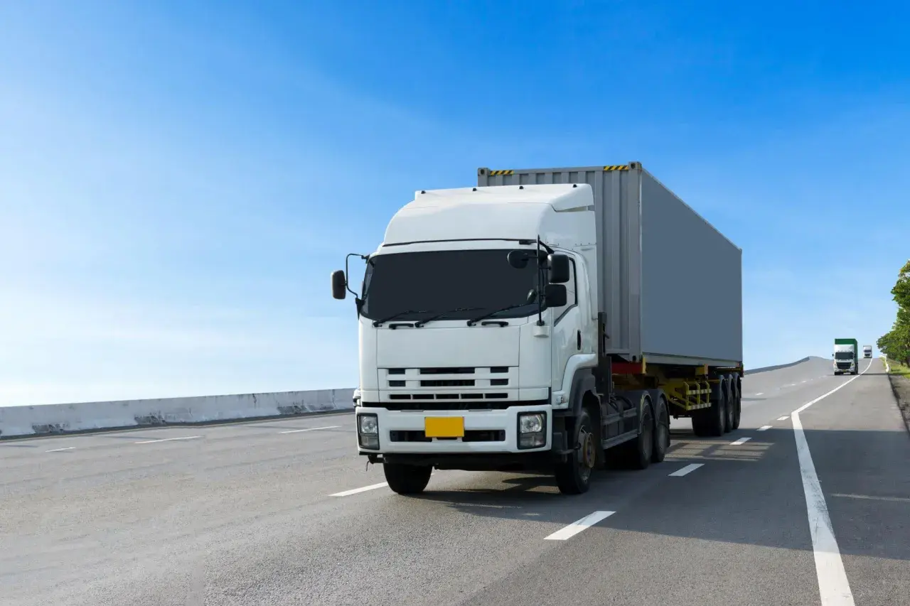 Biały tir z kontenerem jedzie autostradą. Wzór umowy zlecenie dla kierowcy tira jest dostępny online.
