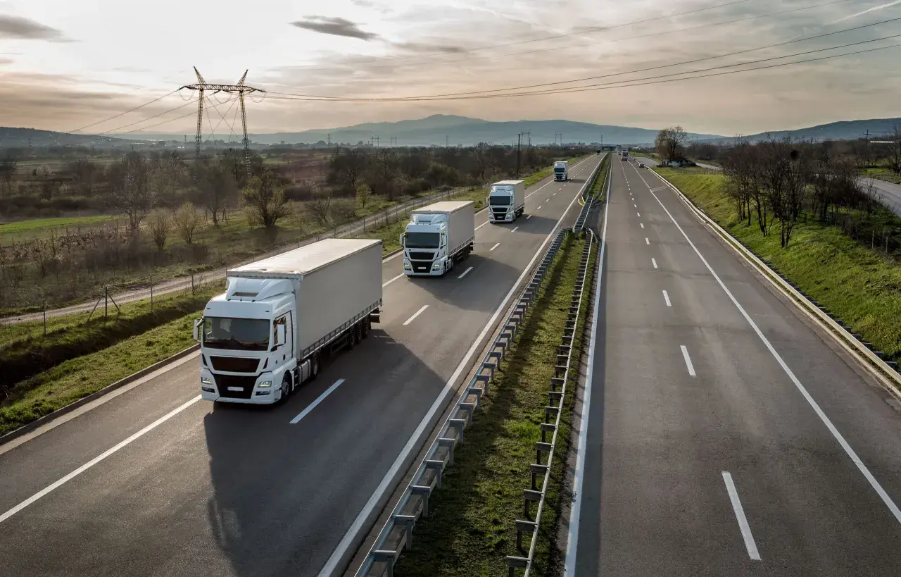 Ciężarówki jadące autostradą, zjazd na bazę pakiet mobilności. W tle góry i linie energetyczne.