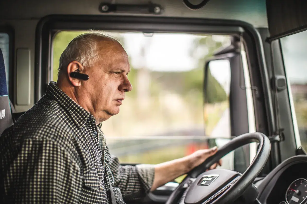 Kierowca ciężarówki w słuchawce Bluetooth, skupiony na drodze. Przestrzega rozporządzenie 561 czas pracy kierowców, dbając o bezpieczeństwo.
