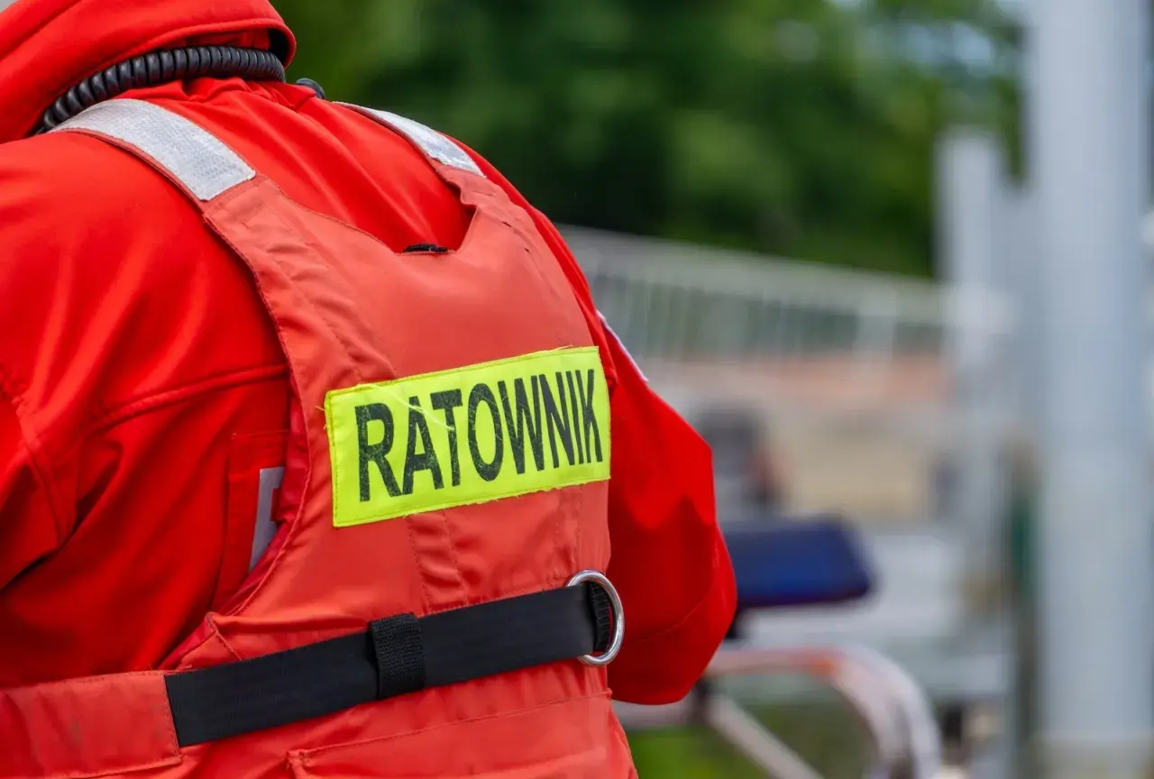 Ratownik w czerwonym stroju, z napisem "RATOWNIK" na kamizelce. Może to być sytuacja, gdy ktoś próbuje kierować ruchem bez uprawnień, a ratownik jest na miejscu.