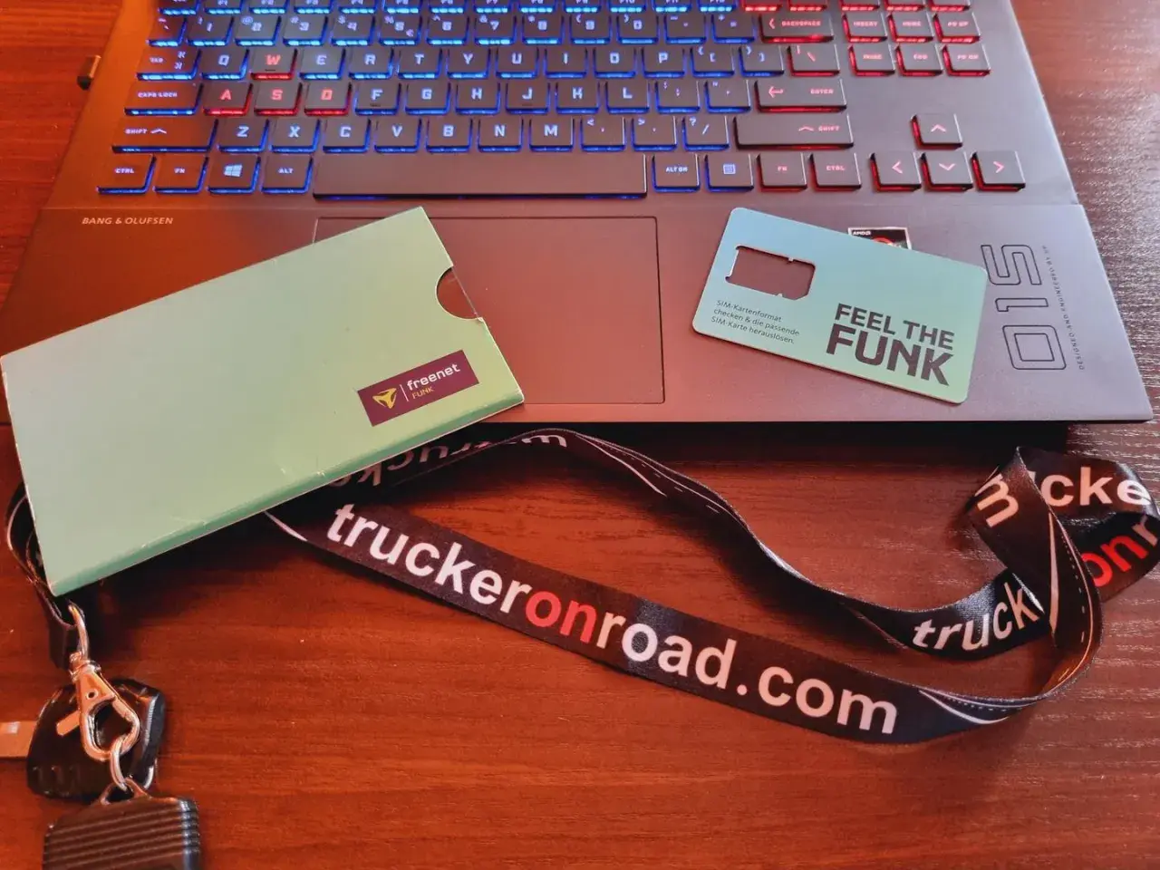 Karta SIM "Feel the Funk" i klucze na smyczy "truckeronroad.com" leżą obok laptopa. Czas na pauzę 45h bez karty w tachografie.