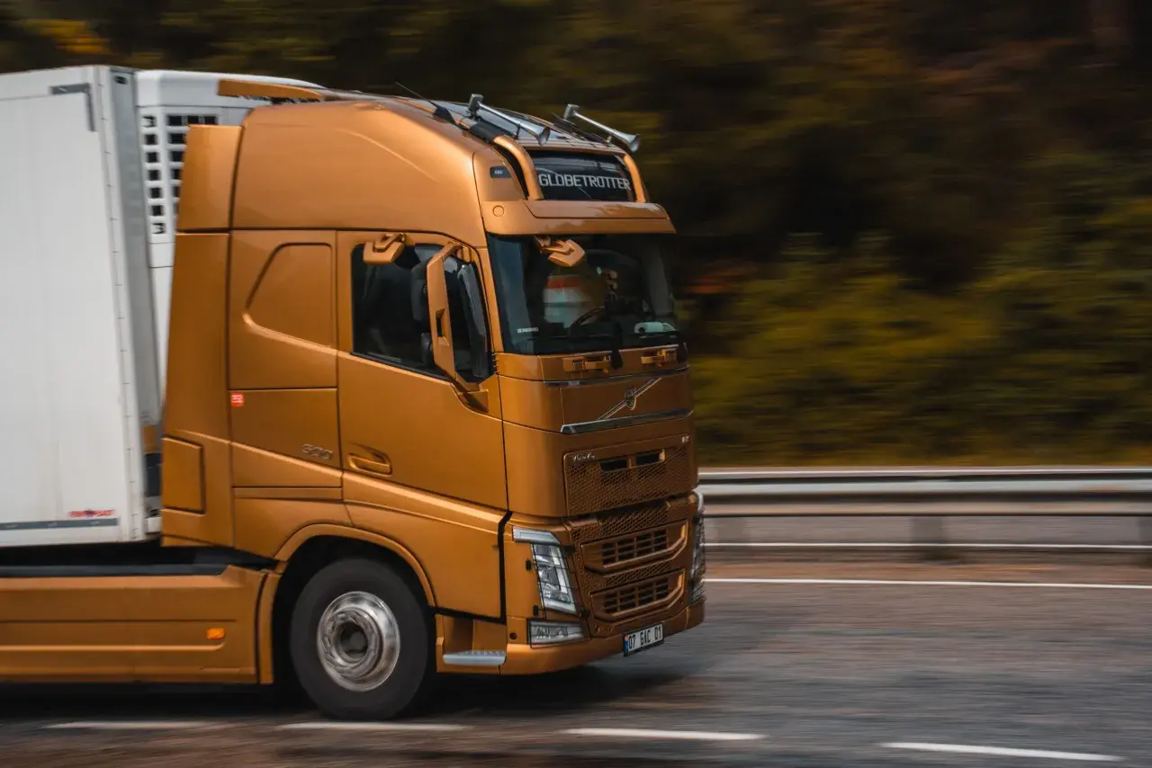 Złoty ciągnik siodłowy z naczepą jedzie drogą. Prawo przewozowe reguluje takie transporty, zapewniając bezpieczeństwo i płynność ruchu.