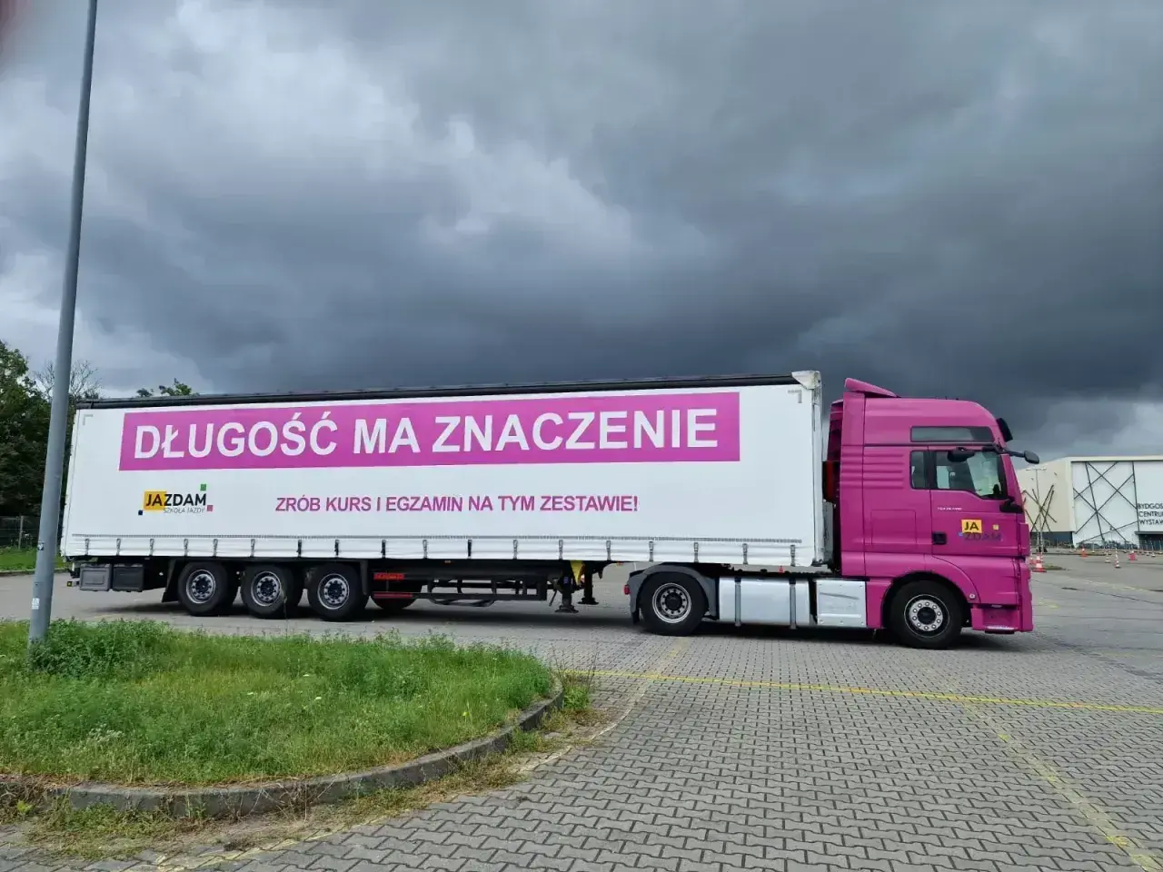 Różowa ciężarówka z napisem "Długość ma znaczenie. Zrób kurs i egzamin na tym zestawie!" zachęca do **testów na przewóz rzeczy**.