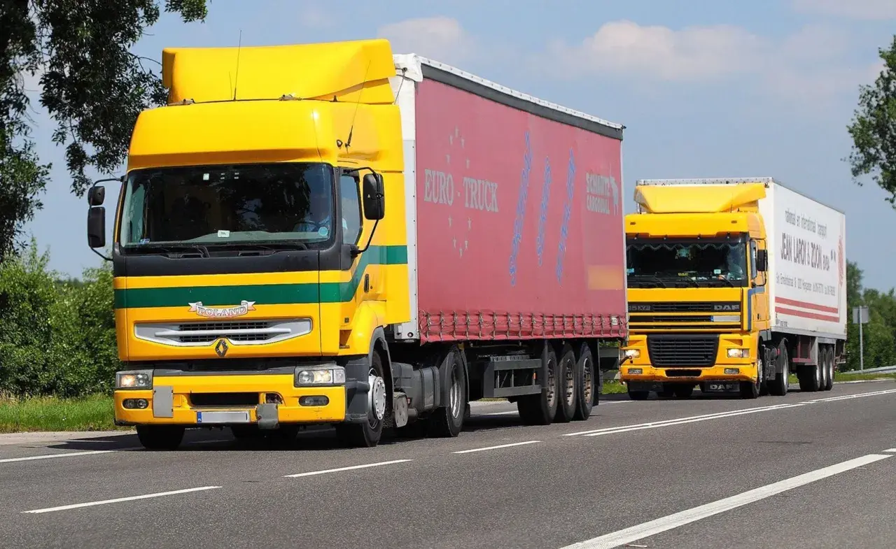 Dwa żółte ciężarówki jadące drogą. Kierowcy wykonujący przewozy drogowe powinni wiedzieć, ile godzin trwa szkolenie okresowe.
