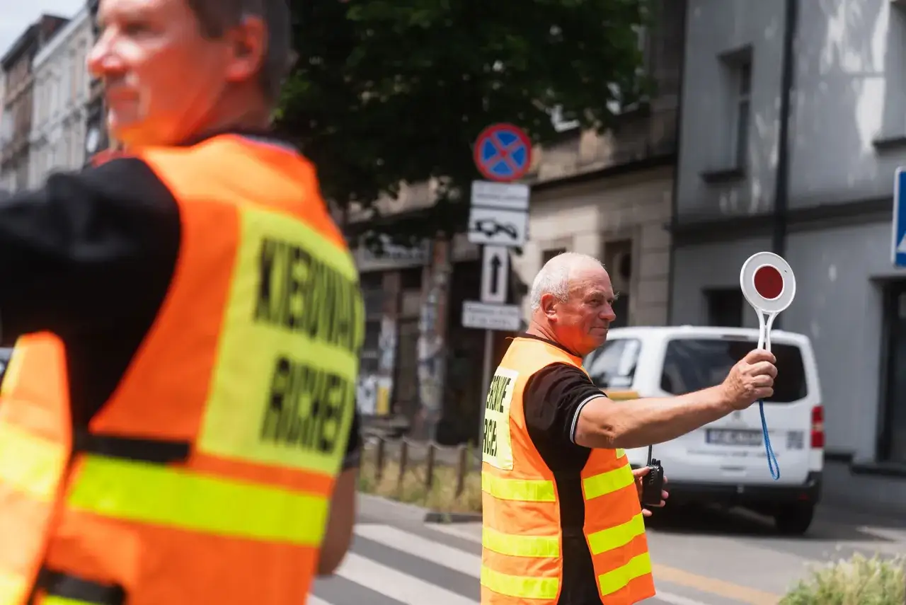Mężczyzna w kamizelce odblaskowej kieruje ruchem. Może to być mandat za kierowanie ruchem bez uprawnień, jeśli nie ma odpowiednich zezwoleń.
