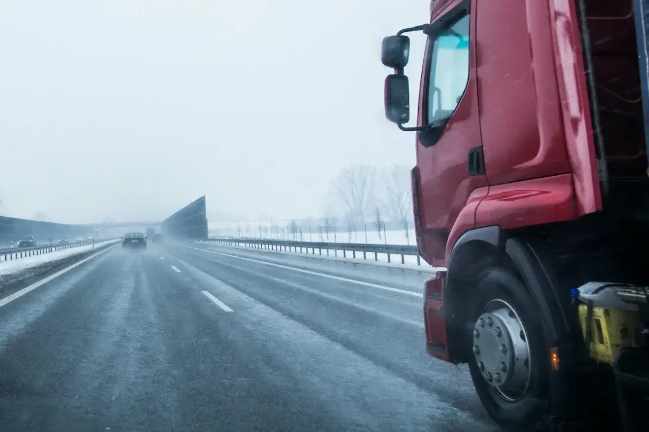 Czerwony tir na mokrej autostradzie w zimowy dzień. Kierowca zastanawia się, ile zarabia kierowca tira z własnym samochodem.