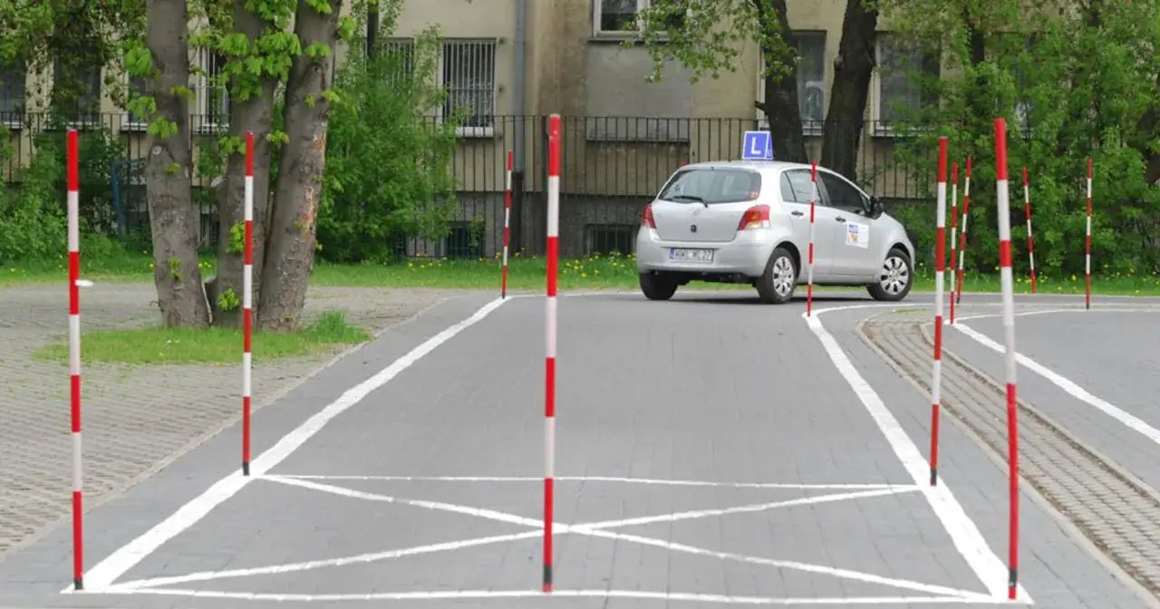 Plac manewrowy z tyczkami i samochodem z literą L. Idealne miejsce na kurs doszkalający dla kierowc&oacute;w kat B.