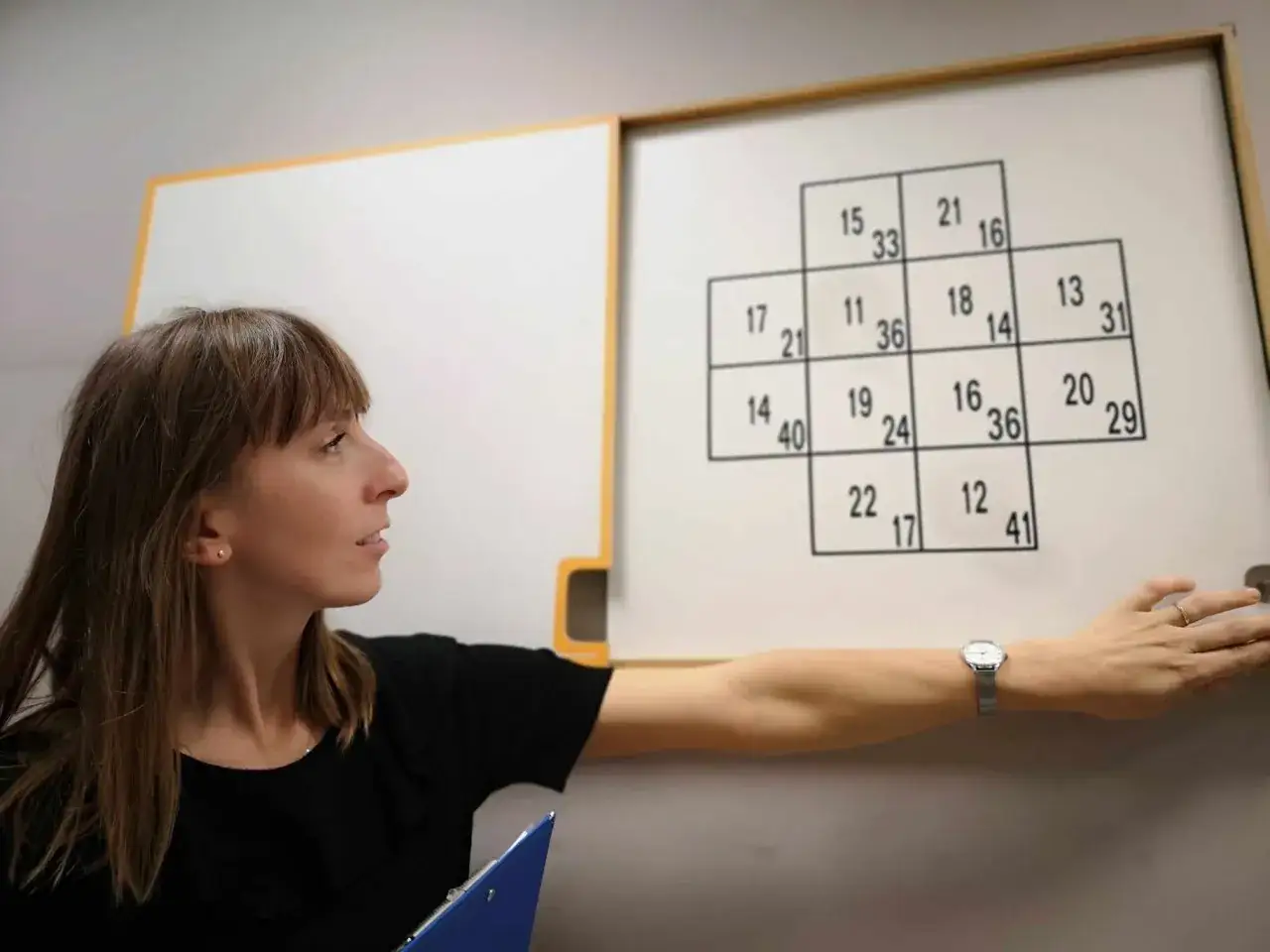 Psycholog prowadzi badania psychologiczne na prawo jazdy, wskazując na tablicę z liczbami.