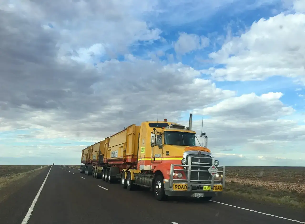 Długi, żółty road train przemierza pustą drogę. To typowa dniówka kierowcy tira na odludziu.