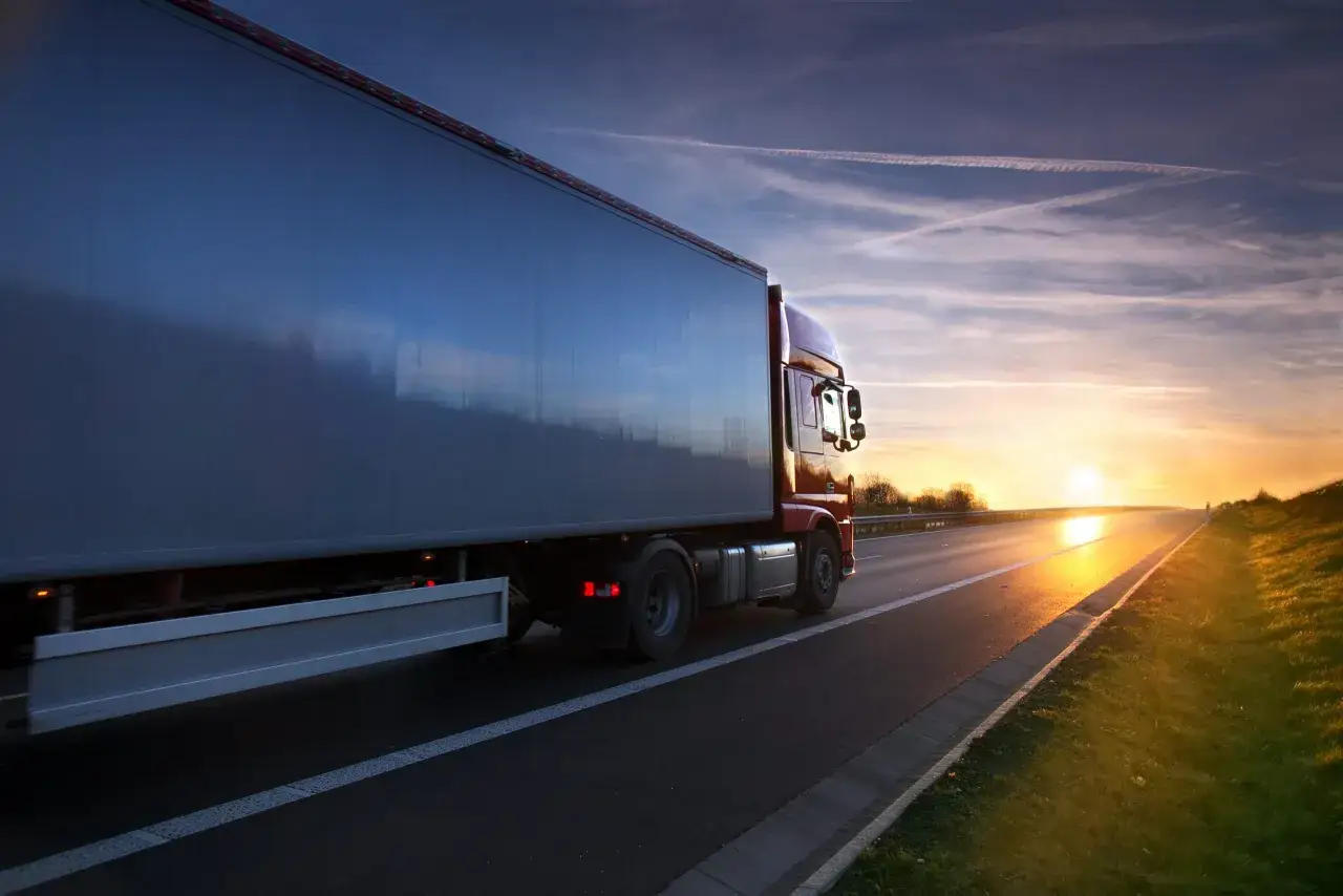 Ciężarówka jedzie autostradą o zachodzie słońca. Kierowca zawodowy wyrusza w długą trasę, by dostarczyć towar.