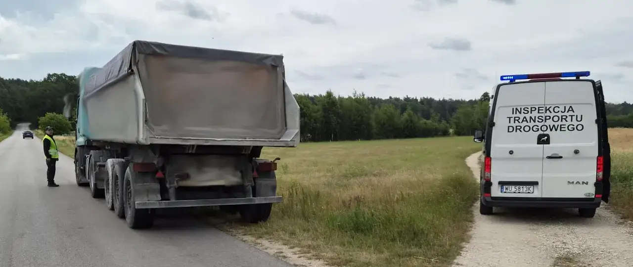 Inspektor drogowy kontroluje ciężarówkę na drodze. Obok stoi biały bus ITD z napisem 