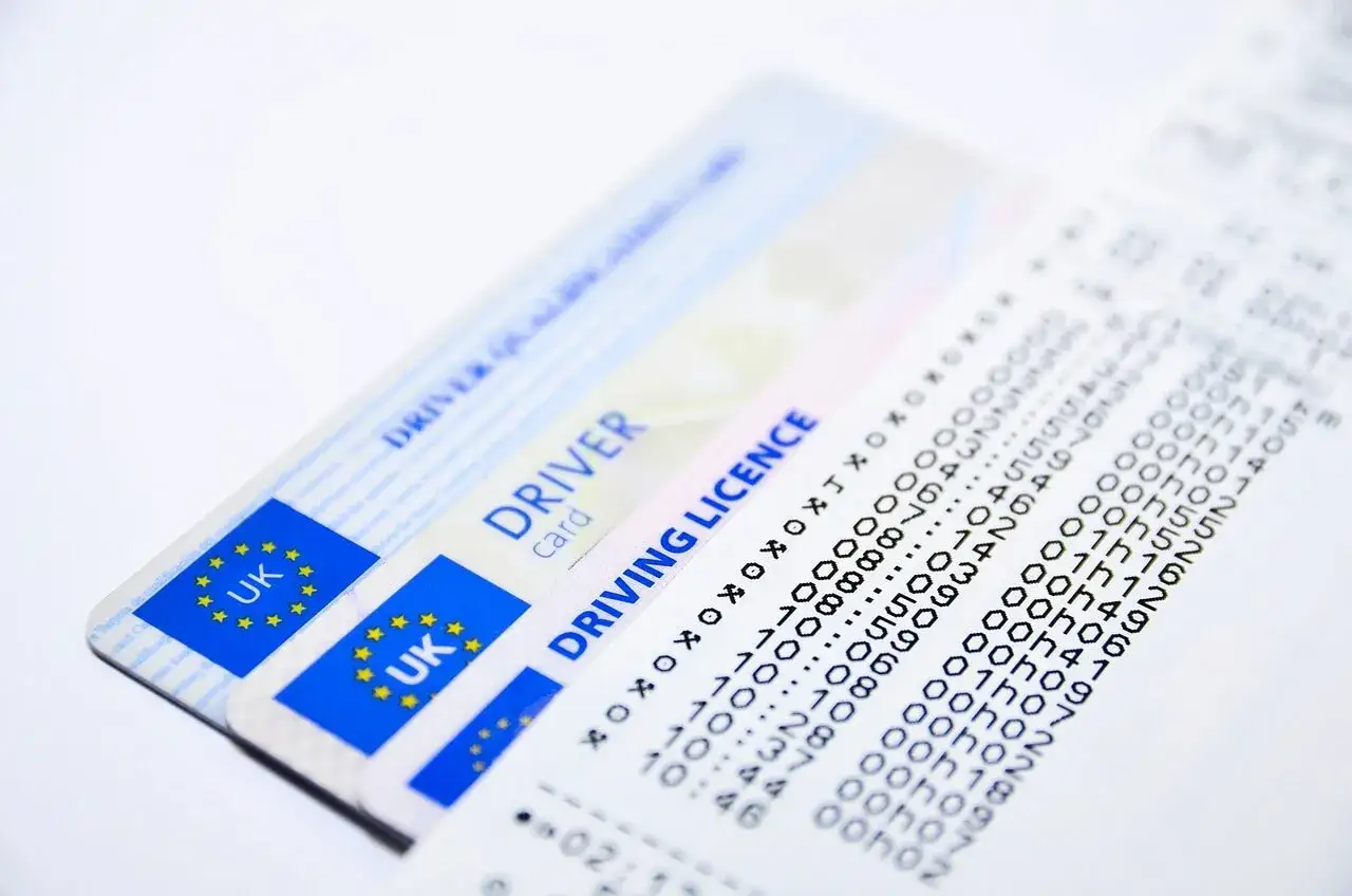 Dwa brytyjskie prawa jazdy i wydruk z tachografu. Druk na kartę kierowcy jest kluczowy dla dokumentacji czasu pracy.