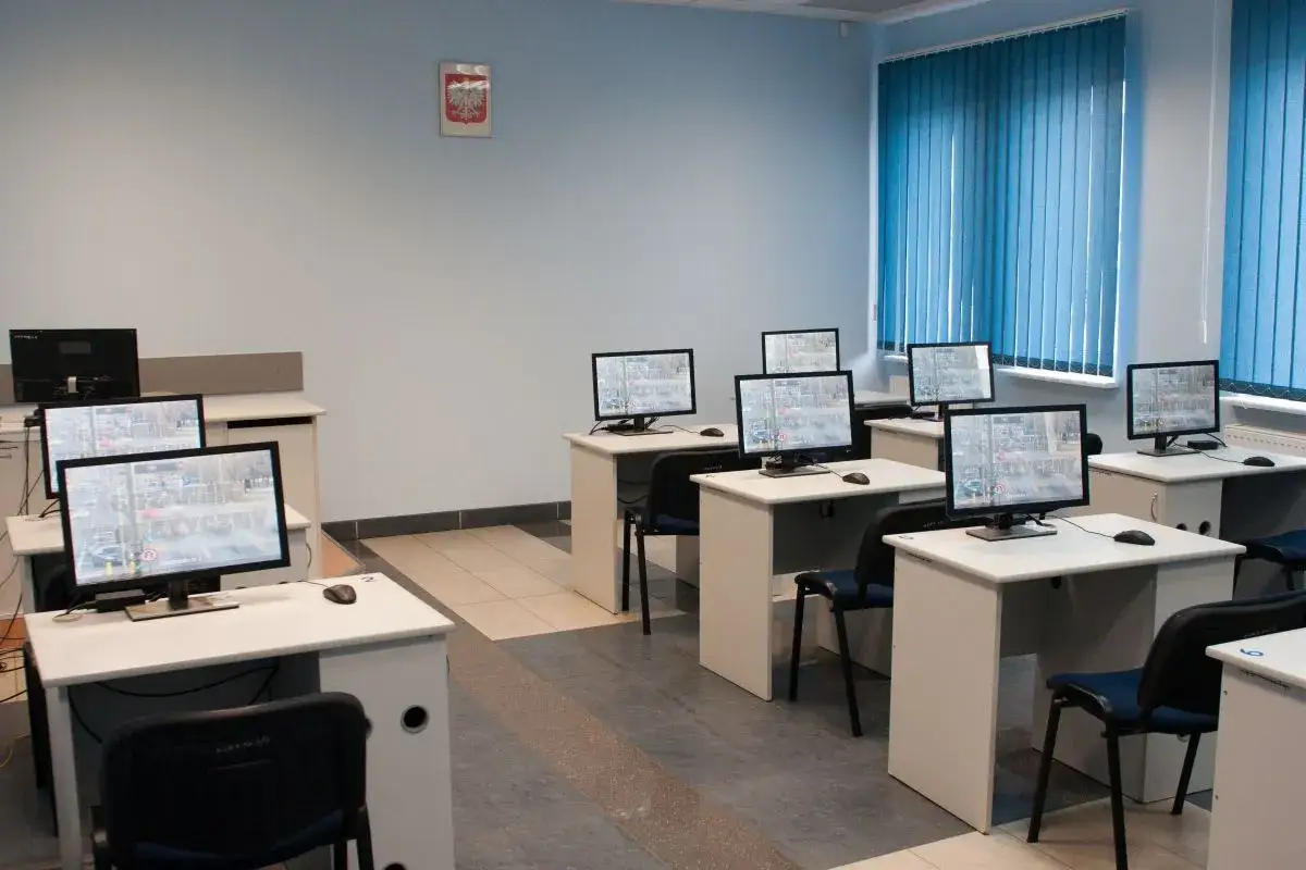Sala komputerowa z wieloma stanowiskami, gdzie odbywa się kwalifikacja wstępna przyspieszona. Testy i odpowiedzi na ekranach.